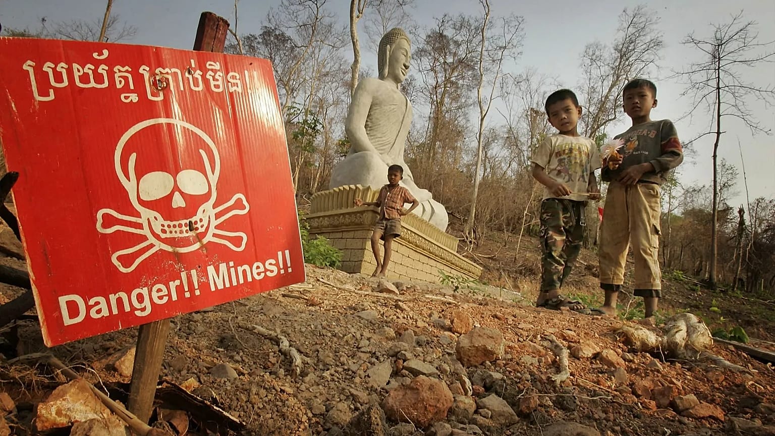 Children play near a landmine warning and a Buddhist shrine in New Village Border, 10 March, 2005