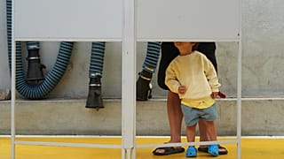 Uma criança observa um eleitor preencher o seu boletim de voto nas eleições gerais de Portugal, numa assembleia de voto em Lisboa, no domingo, 18 de maio de 2025. 