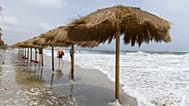 La gente camina por una playa desierta mientras las olas alcanzan las sombrillas de paja en Ibiza, España, el domingo 3 de septiembre de 2023.