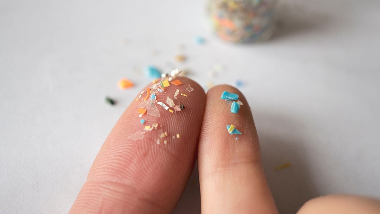 Tiny plastic particles are shown on fingertips.