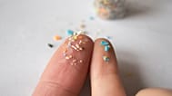 Tiny plastic particles are shown on fingertips.