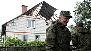 Funkcjonariusze obrony terytorialnej stoją przy uszkodzonym domu, po tym jak rosyjskie drony naruszyły polską przestrzeń powietrzną podczas ataku na Ukrainę