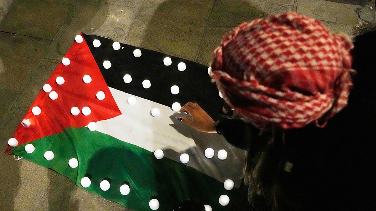 Mulher coloca velas em cima de uma bandeira palestiniana em Roma