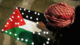 Mulher coloca velas em cima de uma bandeira palestiniana em Roma