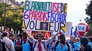 A demonstrator displays a poster of luxury group LVMH CEO Bernard Arnault reading: "B Arnault uses 6 tax havens, thief." 2 Oct. 2025.