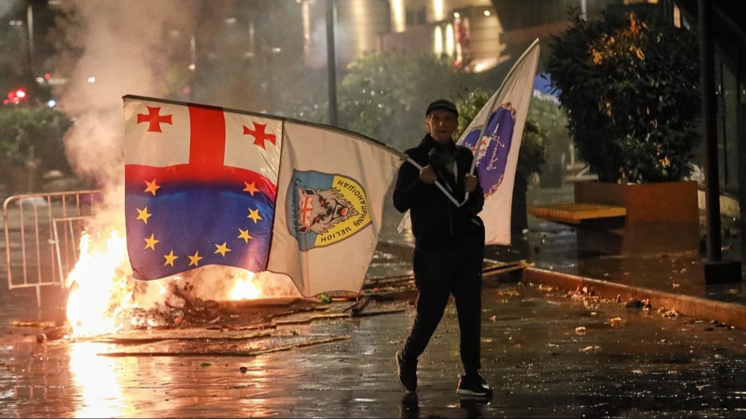 A protester with a Georgian national, EU and other flags walks in front of police line during an opposition rally in Tbilisi, Georgia, on Saturday, Oct. 4, 2025