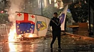 A protester with a Georgian national, EU and other flags walks in front of police line during an opposition rally in Tbilisi, Georgia, on Saturday, Oct. 4, 2025