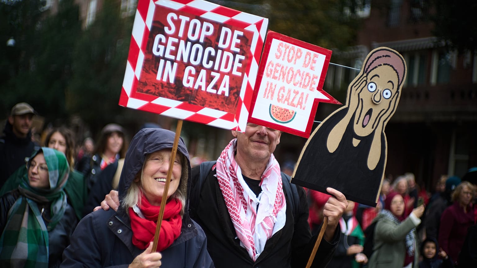 Two people with signs reading "Stop the Genocide in Gaza"