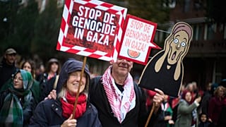 Two people with signs reading "Stop the Genocide in Gaza"