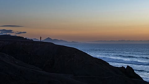 A man watches the sunset over the Atlantic Ocean at the La Pared beach on the Canary Island of Fuerteventura, Spain, Monday, Oct. 6, 2025. 