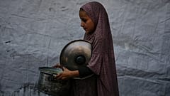 Uma criança palestiniana carrega um pote de comida doada de uma cozinha comunitária em Deir al-Balah, no sul da Faixa de Gaza, a 6 de setembro de 2025.