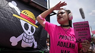 An activists holds a poster as a flag bearing an image of skull with straw hat from the popular Japanese anime One Piece
