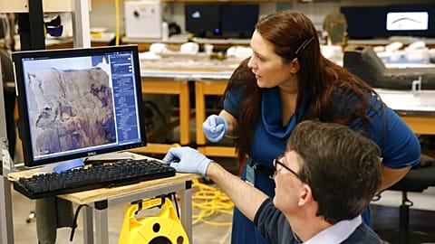 صورة تعبيرية لعالم آثار ومساعدته يفحصان صورةً للجزء الخلفي من مومياء مينيرديس