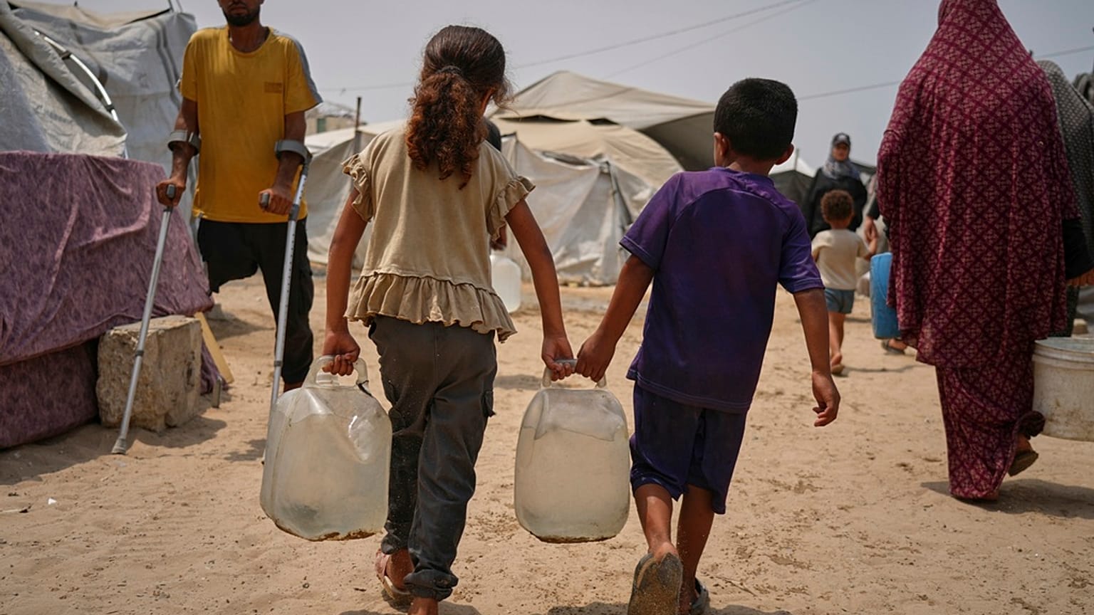 أطفال فلسطينيون ينقلون عبوات مياه تم جمعها من نقطة توزيع في مدينة غزة، 12 أغسطس/آب 2025