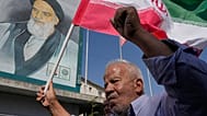 يقف مصلٍّ إيراني ممسكًا بعلم بلاده أمام صورة للراحل مؤسس الثورة آية الله الخميني