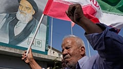 يقف مصلٍّ إيراني ممسكًا بعلم بلاده أمام صورة للراحل مؤسس الثورة آية الله الخميني