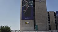Persone passano davanti a un grande schermo all'aperto che mostra un'immagine del Presidente degli Stati Uniti Donald Trump, a Gerusalemme, sabato 11 ottobre 2025, dopo che Israele e Hamas hanno concordato un accordo di pace. 