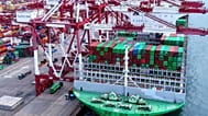 Trucks move by a vessel docked at a container terminal in Qingdao in east China's Shandong province, Monday, Aug. 11, 2025.