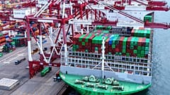 Des camions circulent près d'un navire amarré à un terminal à conteneurs à Qingdao, dans la province de Shandong, dans l'est de la Chine, le lundi 11 août 2025.