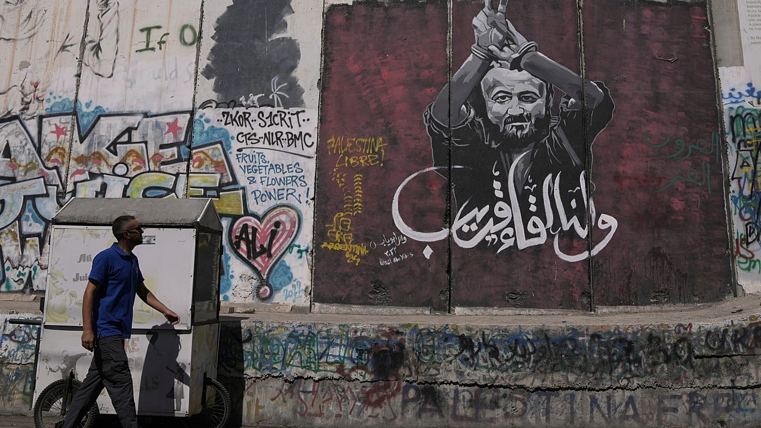رجل يمر بجانب لوحة جدارية تُصوّر الزعيم الفلسطيني مروان البرغوثي، تحمل رسالة مكتوبة بالعربية تقول: "أراك قريبًا".