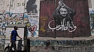 رجل يمر بجانب لوحة جدارية تُصوّر الزعيم الفلسطيني مروان البرغوثي، تحمل رسالة مكتوبة بالعربية تقول: "أراك قريبًا".