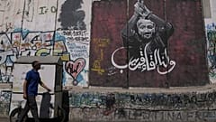 رجل يمر بجانب لوحة جدارية تُصوّر الزعيم الفلسطيني مروان البرغوثي، تحمل رسالة مكتوبة بالعربية تقول: "أراك قريبًا".