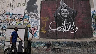 رجل يمر بجانب لوحة جدارية تُصوّر الزعيم الفلسطيني مروان البرغوثي، تحمل رسالة مكتوبة بالعربية تقول: "أراك قريبًا".