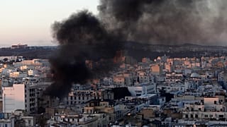 عمود من الدخان يتصاعد من مبانٍ خلال مواجهات بين محتجين والشرطة في العاصمة تونس، الجمعة 14 يناير 2011.