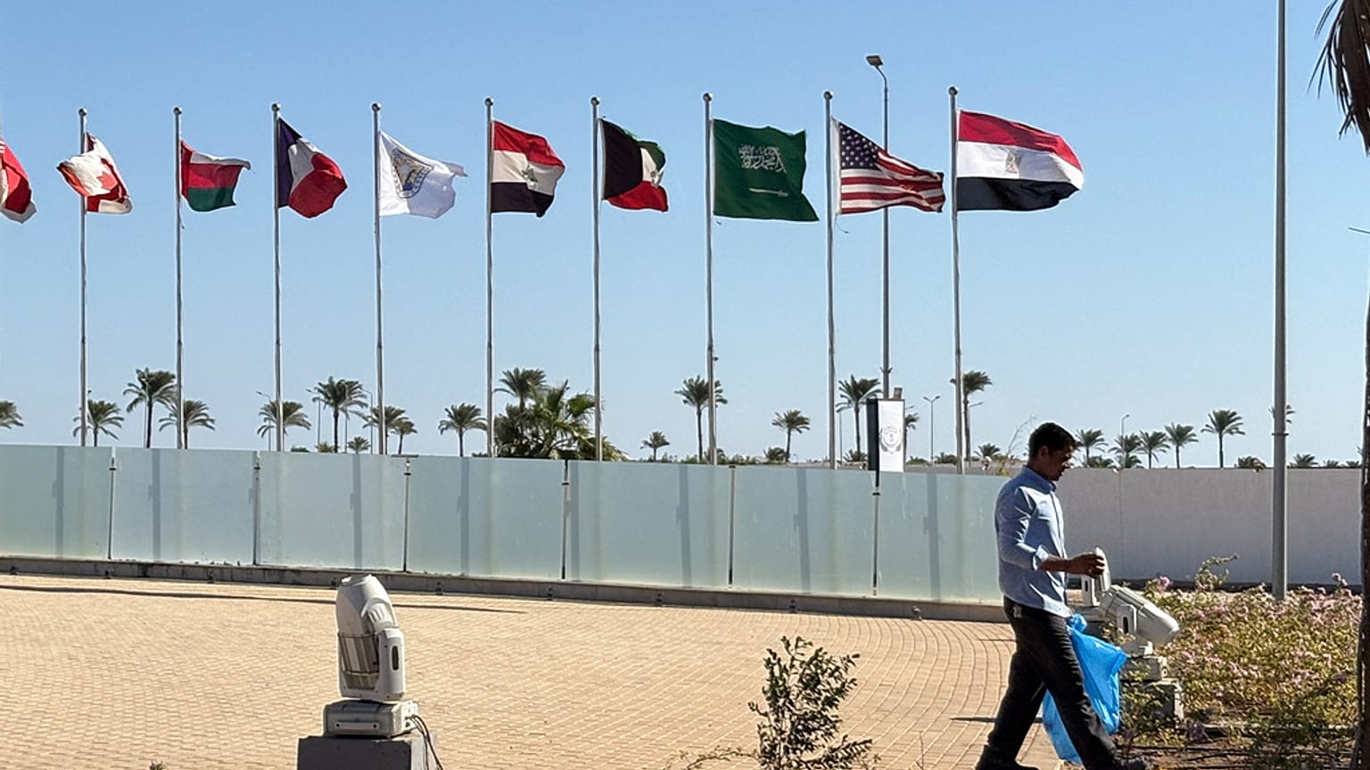  عامل يمشي أمام أعلام الدول المشاركة في القمة التي استضافتها مصر للاحتفال بتوقيع اتفاق وقف إطلاق النار بين إسرائيل وحماس في شرم الشيخ، مصر، الأحد 12 أكتوبر 2025.