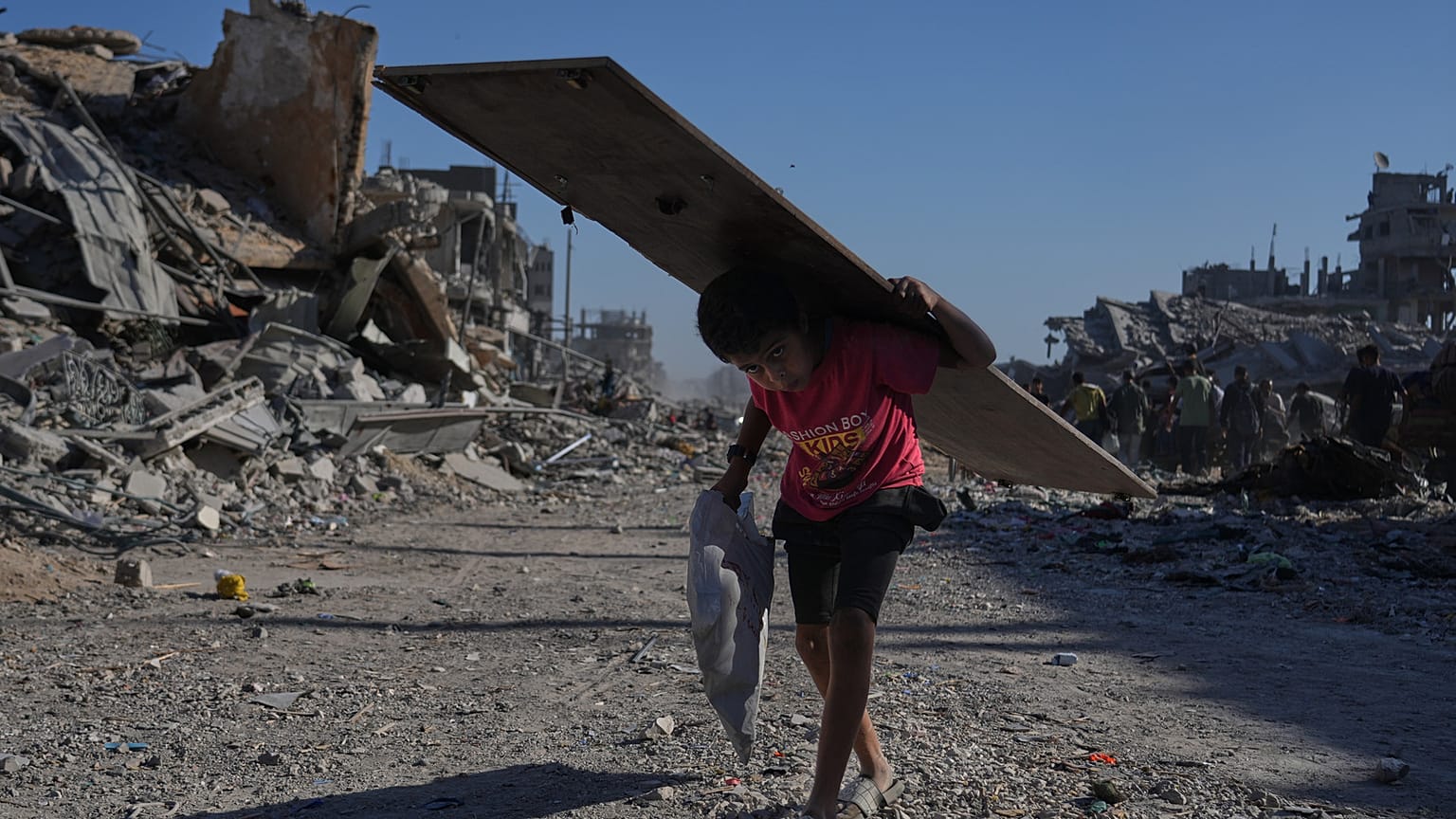 صبي فلسطيني نازح يحمل لوحًا خشبيًا أثناء سيره في شارع الجلاء المتضرر بشدة في مدينة غزة، يوم السبت 11 أكتوبر 2025،