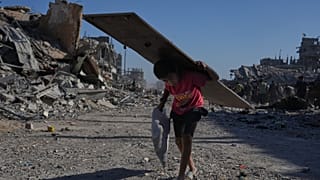 صبي فلسطيني نازح يحمل لوحًا خشبيًا أثناء سيره في شارع الجلاء المتضرر بشدة في مدينة غزة، يوم السبت 11 أكتوبر 2025،
