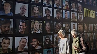Γυναίκες περπατούν μπροστά από ένα πανό με φωτογραφίες ομήρων που απήχθησαν και κρατούνται από τη Χαμάς στη Λωρίδα της Γάζας, στην Ιερουσαλήμ, Τρίτη 7 Οκτωβρίου 2025, στη δεύτερη επέτειο της