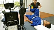 لاعب كرة القدم الأمريكية نات ليتل، مستلقٍ على بساط التدريب بينما تُدرّبه المعالجة الفيزيائية ميشيل مور على ساقيه، يوم الخميس، 8 يوليو/تموز 2004.