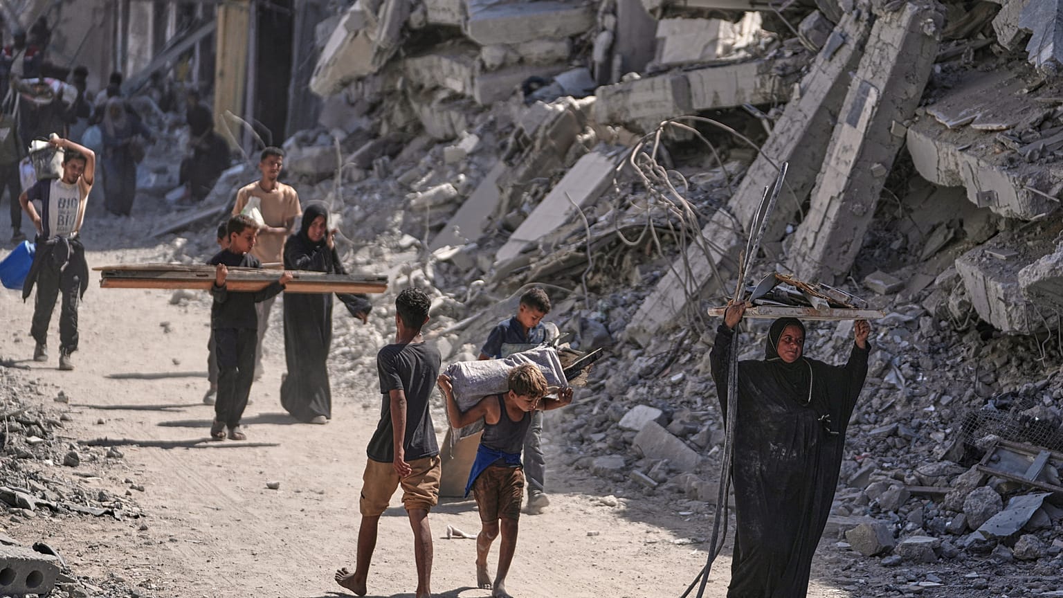 فلسطينيون نازحون يسيرون حامِلين أغراضهم بجانب المباني المدمرة أثناء عودتهم إلى منازلهم في خان يونس.. (تصوير: جيهاد الشرافي/أسوشيتد برس)