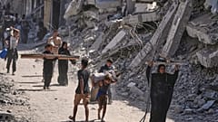 فلسطينيون نازحون يسيرون حامِلين أغراضهم بجانب المباني المدمرة أثناء عودتهم إلى منازلهم في خان يونس.. (تصوير: جيهاد الشرافي/أسوشيتد برس)