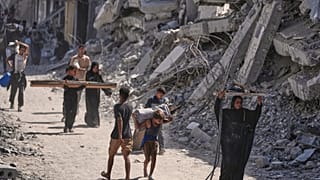 فلسطينيون نازحون يسيرون حامِلين أغراضهم بجانب المباني المدمرة أثناء عودتهم إلى منازلهم في خان يونس.. (تصوير: جيهاد الشرافي/أسوشيتد برس)