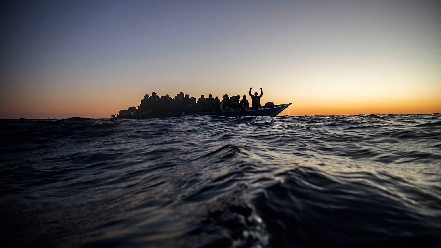 Migrants and refugees wait for assistance on an overcrowded wooden boat, as aid workers approach them in the Mediterranean Sea off the Libyan coast, 12 February 2021