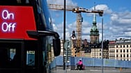 A food delivery courier rides a bicycle past a construction site's fence, with the German Church in the background, in Stockholm, 27 July 2023