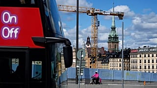 A food delivery courier rides a bicycle past a construction site's fence, with the German Church in the background, in Stockholm, 27 July 2023