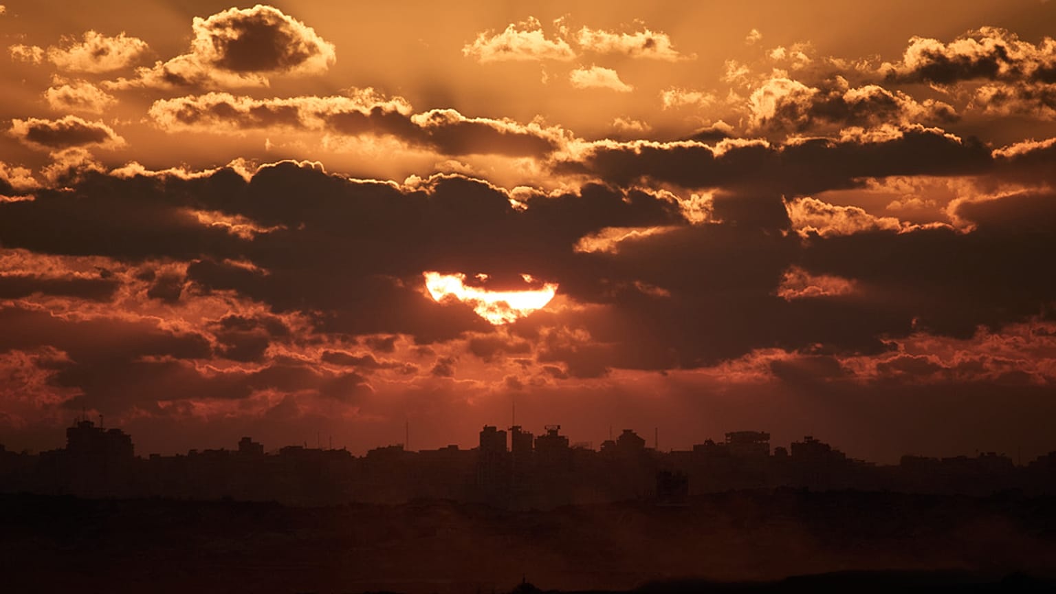 تغيب الشمس خلف المباني المدمرة  في شمال قطاع غزة، كما يُرى من جنوب إسرائيل، الثلاثاء 14 أكتوبر 2025.