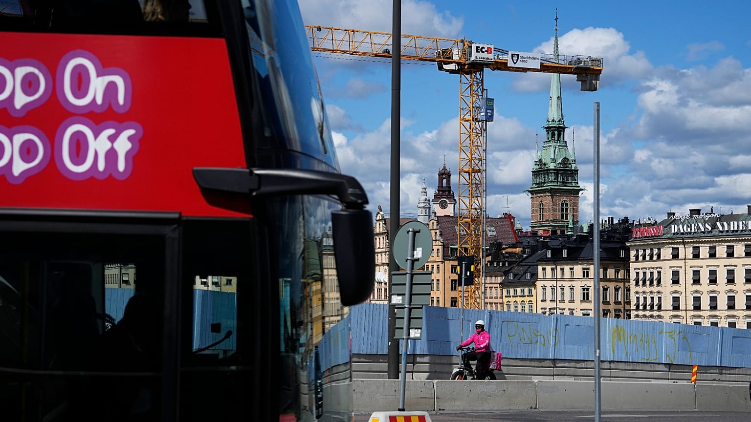 Um entregador de comida passa de bicicleta pela cerca de um canteiro de obras, com a Igreja Alemã ao fundo, em Estocolmo, em 27 de julho de 2023.