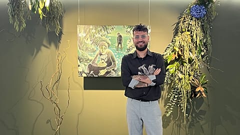 Cem Güventürk yeni sergisindeki eserlerden birinin önünde poz veriyor.
