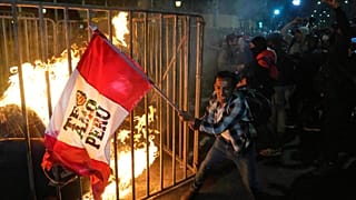 Un manifestante ondea una bandera peruana mientras una muñeca de cartón arde frente al Congreso