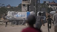  فلسطينيون يسارعون نحو الشاحنات التي تحمل مساعدات من برنامج الغذاء العالمي أثناء مرورها بدير البلح في وسط غزة، الأربعاء 15 أكتوبر/تشرين الأول 2025. 