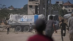  فلسطينيون يسارعون نحو الشاحنات التي تحمل مساعدات من برنامج الغذاء العالمي أثناء مرورها بدير البلح في وسط غزة، الأربعاء 15 أكتوبر/تشرين الأول 2025. 