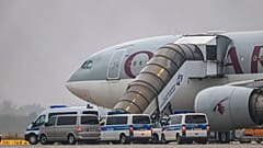 Люди садятся на самолет Qatar Airways, перед которым стоят машины федеральной полиции, на взлетной полосе аэропорта Лейпциг/Галле, пятница, 18 июля 2025 года, Саксония, Шкойдитц.