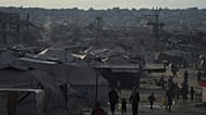 فلسطينيون نازحون يتجولون في مخيم خيام مجاور للمنازل والمباني المدمرة في خان يونس بقطاع غزة، السبت 18 أكتوبر 2025. 