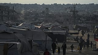 فلسطينيون نازحون يتجولون في مخيم خيام مجاور للمنازل والمباني المدمرة في خان يونس بقطاع غزة، السبت 18 أكتوبر 2025. 
