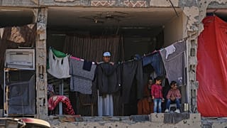 Palestinianos observam membros do grupo militante Hamas à procura dos corpos dos reféns israelitas em Khan Younis, no sul da Faixa de Gaza, domingo, 19 de outubro de 2025