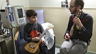 يتلقى جاريد أماند درسًا في الموسيقى من كيفن سميث من مؤسسة Snow City Arts، في مستشفى سنترال دوباج في وينفيلد، إلينوي